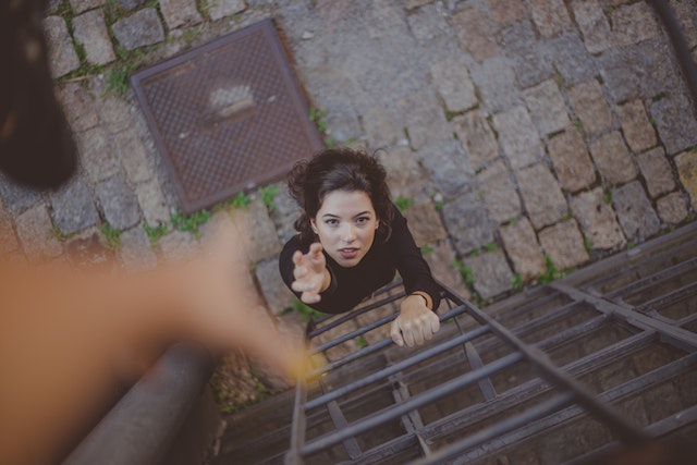 A woman climbs a ladder, reaching for help from above