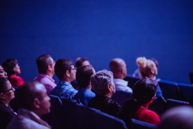 An audience sits listening at a conference.