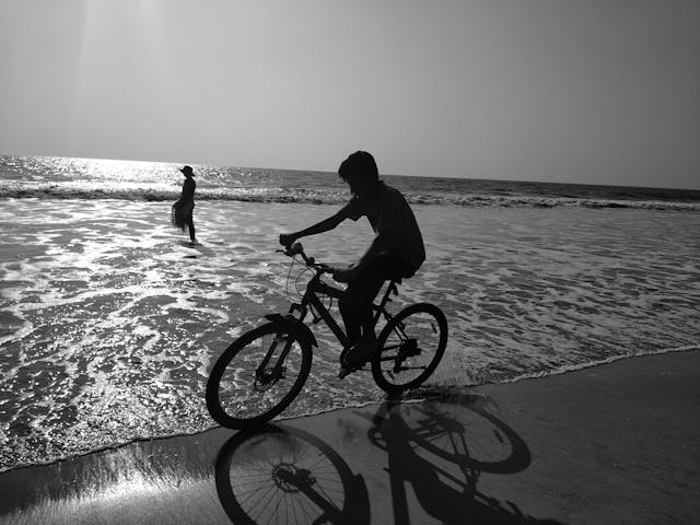 A man cycles a bicyle across a beach.