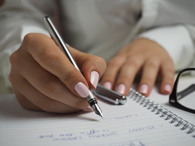 A woman's hands writing in a note book with a pen.