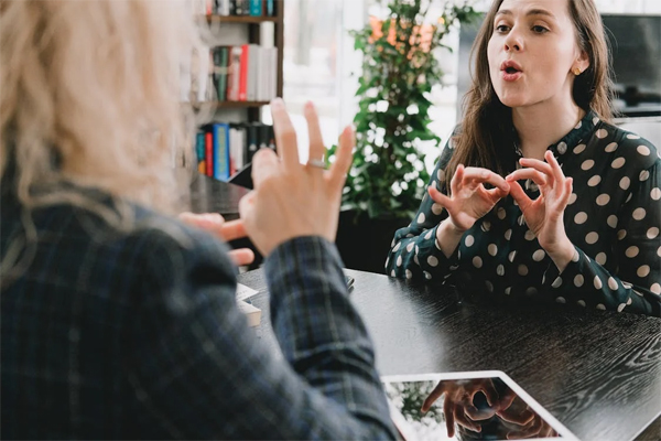 Two women conduct a conversation in sign language while sat at a table.