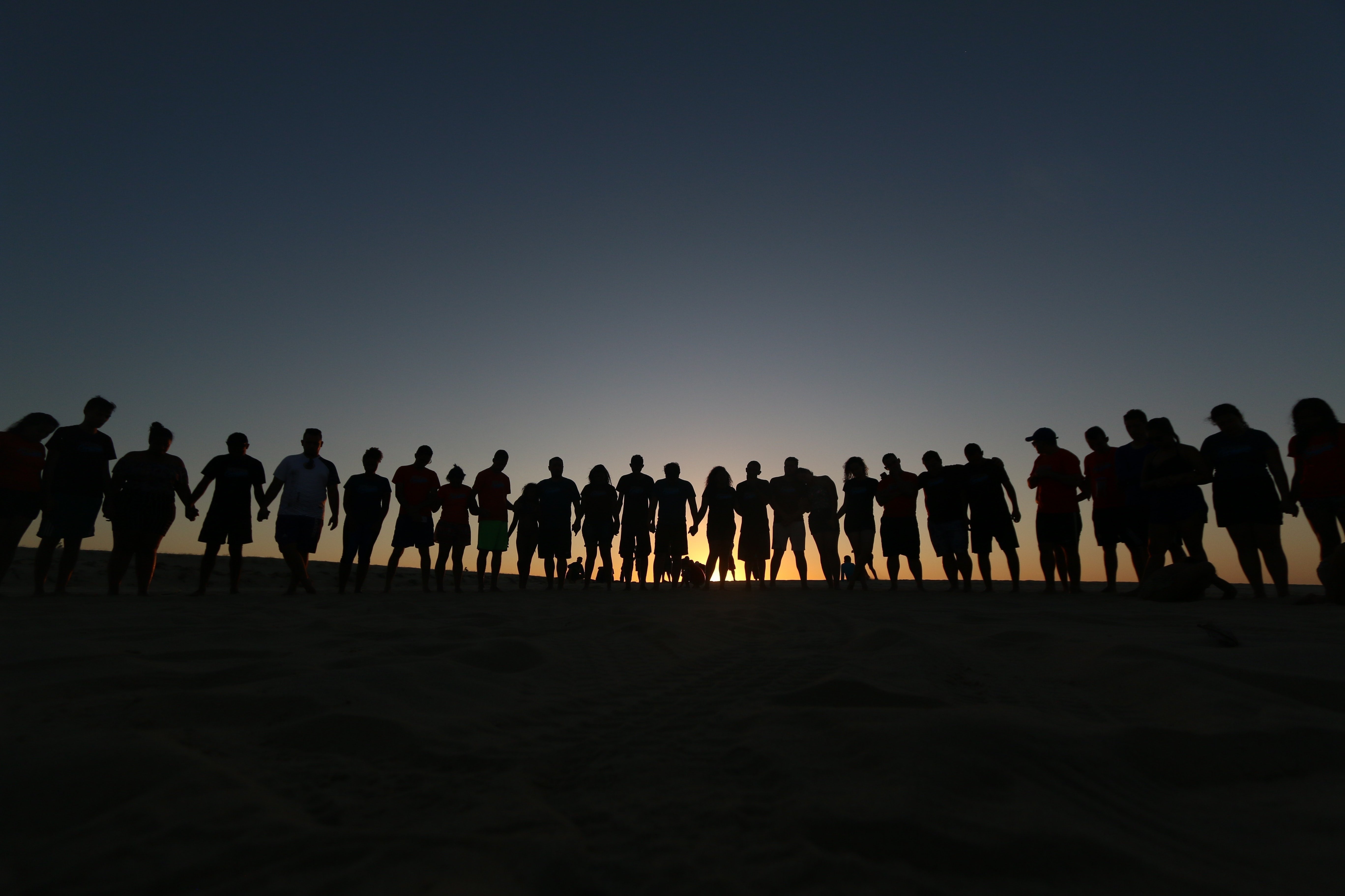 A silhouette of several people standing outside in a straight line, holding hands