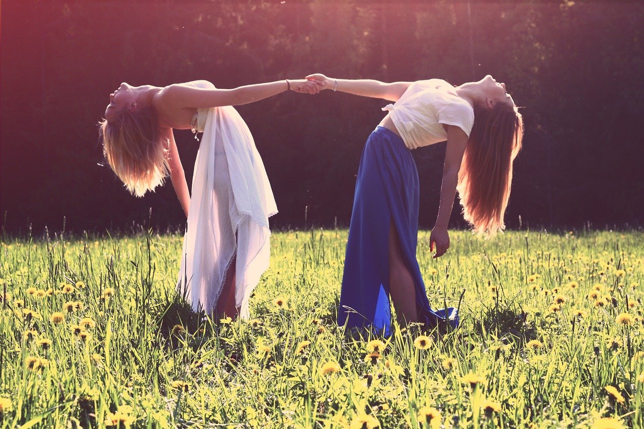 Two women holding hands in a sunny grass field