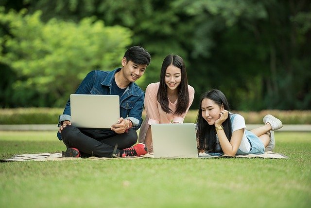 Three students gathered around laptops, in a park