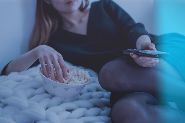A woman watches television while eating popcorn