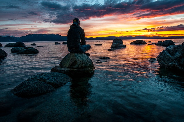 A man sits on a rock overlooking a bay
