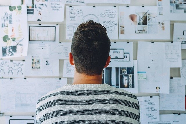 A man stares at a wall covered in pieces of paper with academic writing on them